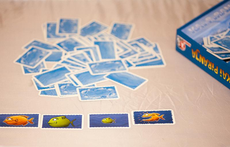 In der Mitte liegen die Spielkarten bunt gemischt mit der Bildseite nach unten. Vor dem Spieler liegen drei aufgedeckte Karten, auf denen Fische abgebildet sind.