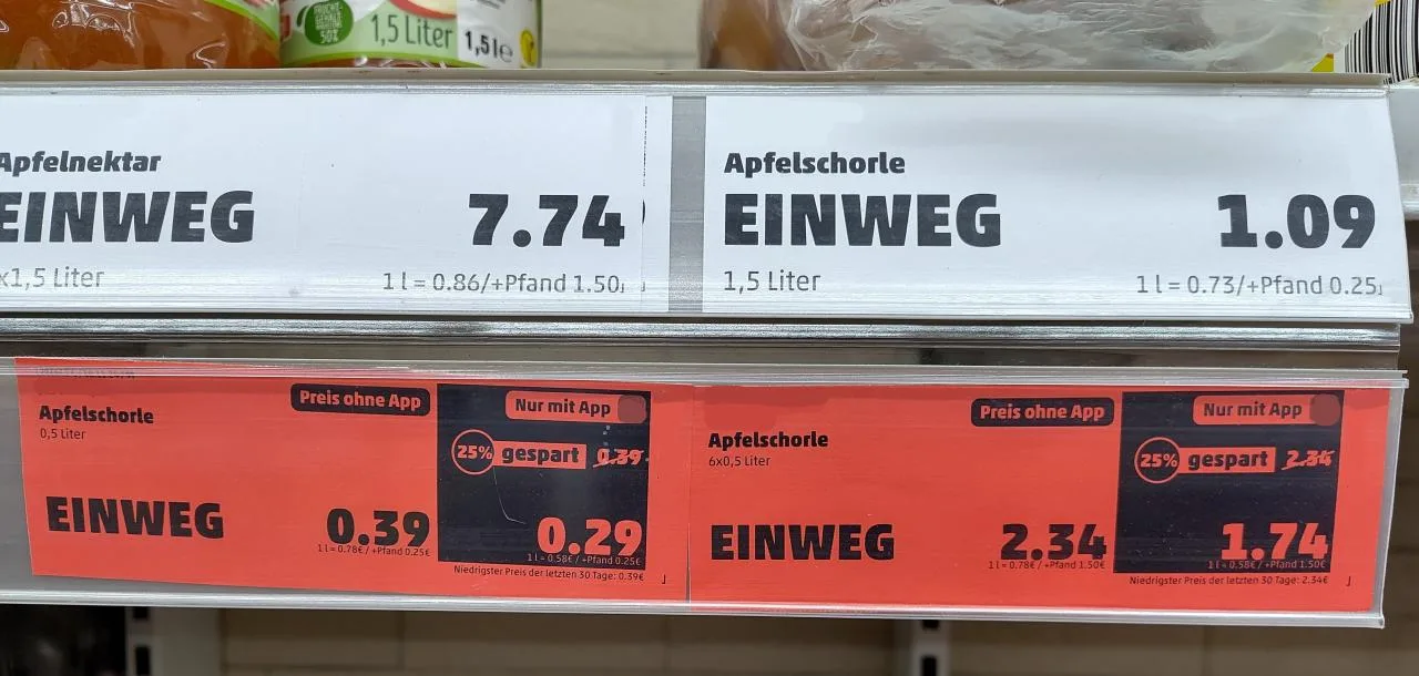 Angebotspreise auf einem roten Ettikett. Apfelschorle 0,5 Liter kostet regulär 0,39 € und mit App 0,29 €. Sechs mal 0,5 Liter kosten regulär 2,34 € und mit App 1,74 €.