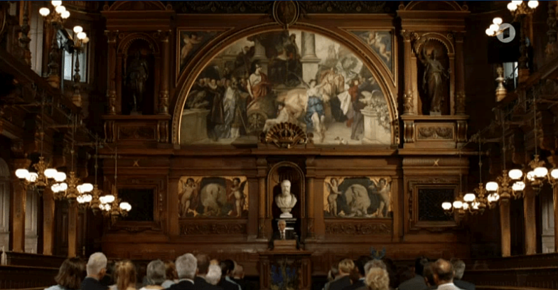 Sprecher zentral, in Historischem Saal mit Publikum.