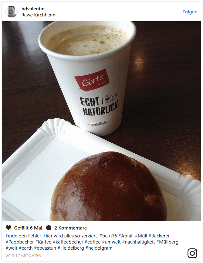 Ein Rosinenbrötchen liegt auf einem Pappteller und der Kaffee ist im Einwegbecher.