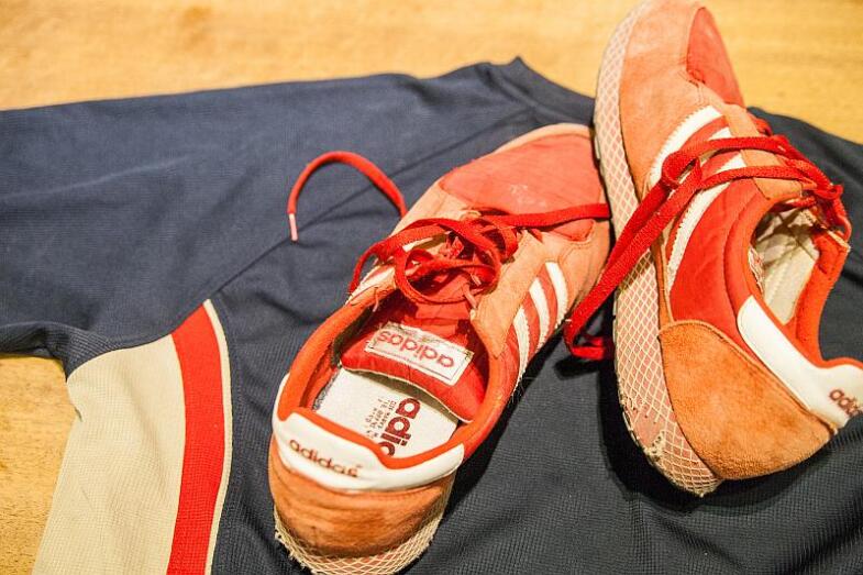 Rote Laufschuhe mit drei weißen Streifen liegen auf einem Laufshirt