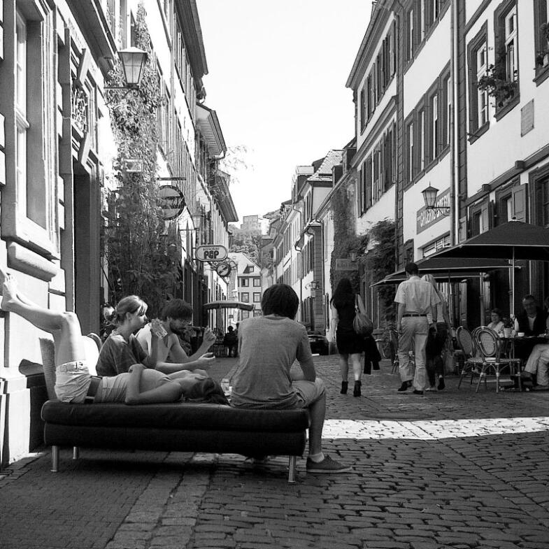 Mitten in der Altstadt haben einige Bewohner ihre Couch auf das Kopfsteinpflaster getragen und lassen sich gemütlich dort nieder - Foto in Schwarz-Weiß