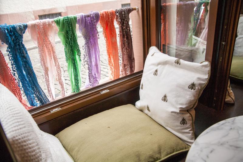 Mit Kissen ausgestaltete Sitzecke auf der Fensterbanck, draußen sind bunte Halstücher angebunden