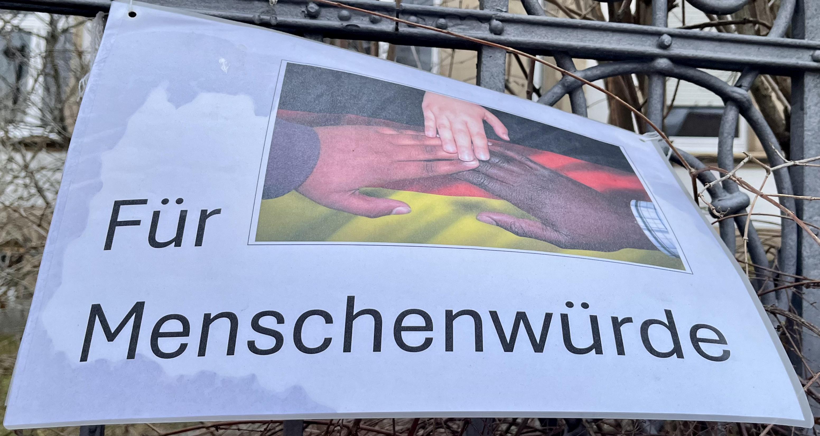 Plakat mit der Aufschrift "Für Menschenwürde", ein Schmuckbild verdeutlicht diesen Text.