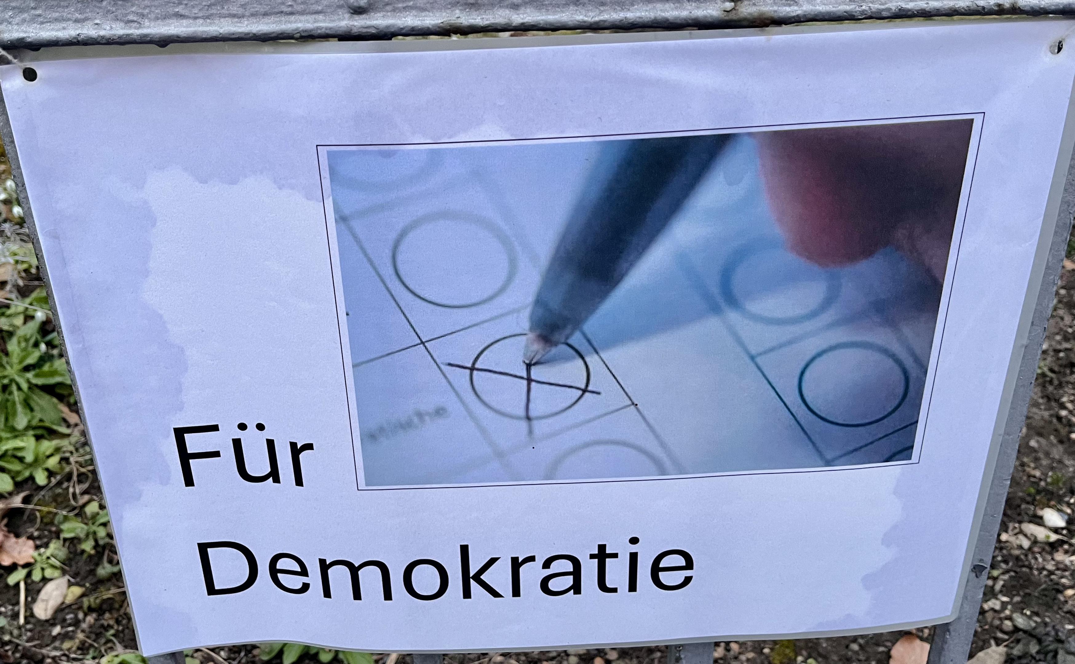 Plakat mit der Aufschrift "Für Demokratie", ein Schmuckbild verdeutlicht diesen Text.