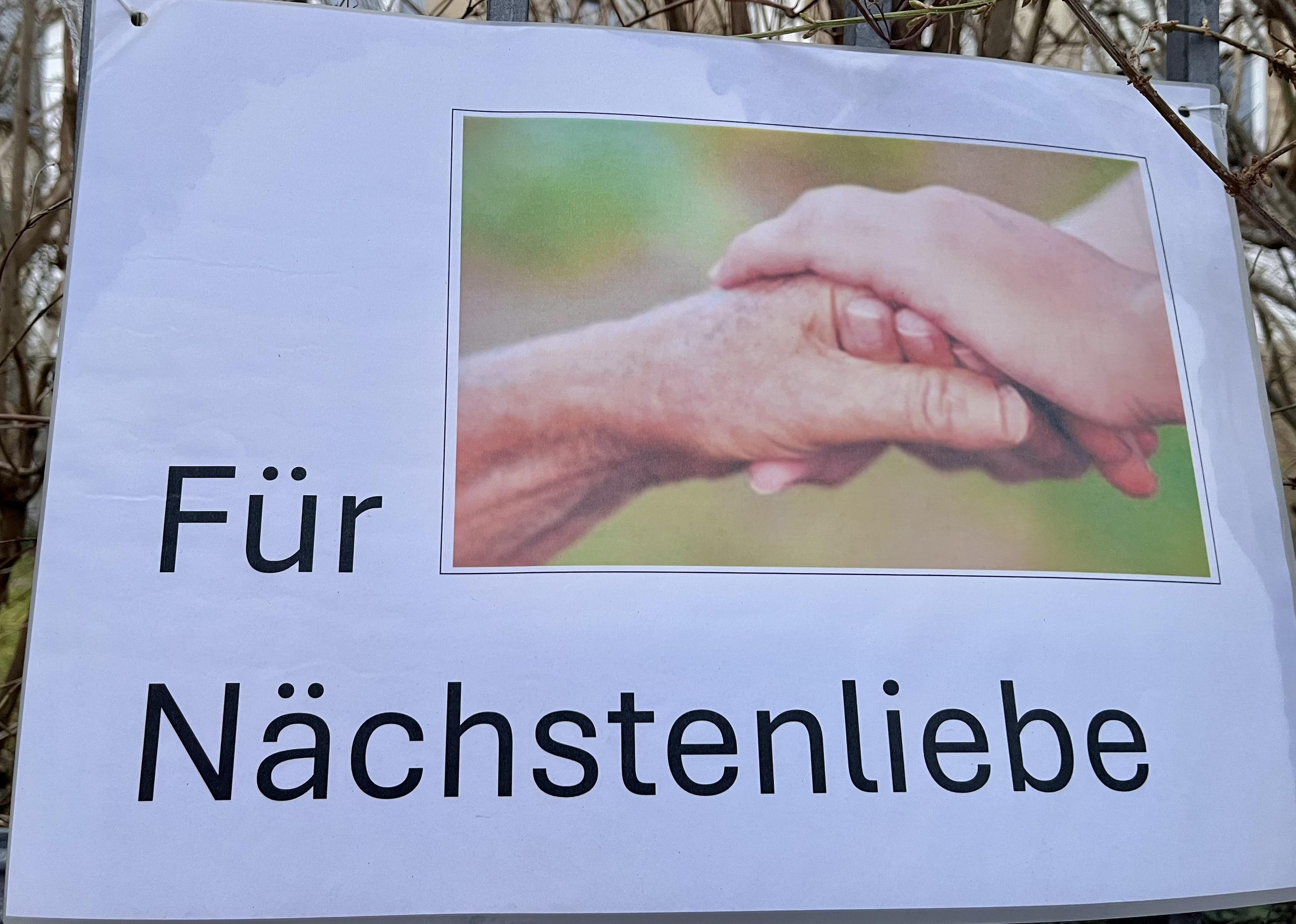Plakat mit der Aufschrift "Für Nächstenliebe", ein Schmuckbild verdeutlicht diesen Text.