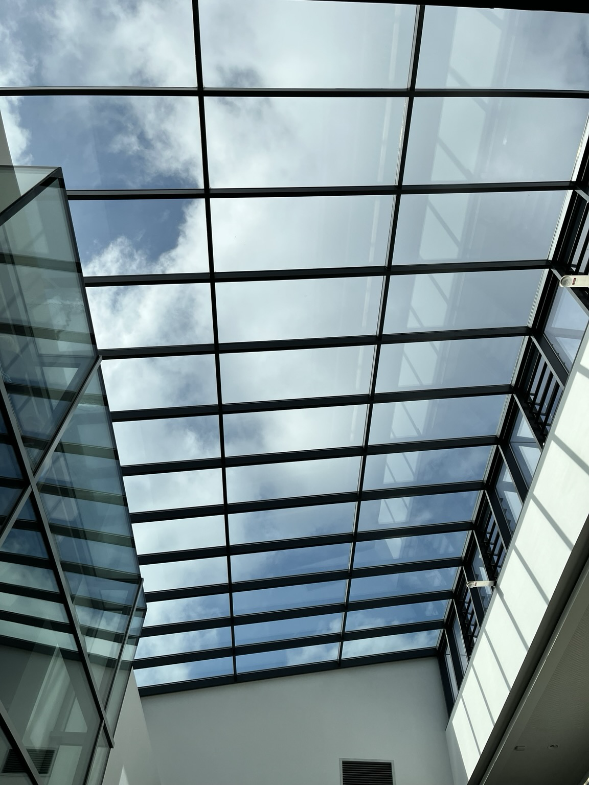 Blick nach oben. Es gibt ein weiteres Stockwerk. Darüber ist durch Fenster der leicht bewölkte Himmel zu erkennen. 