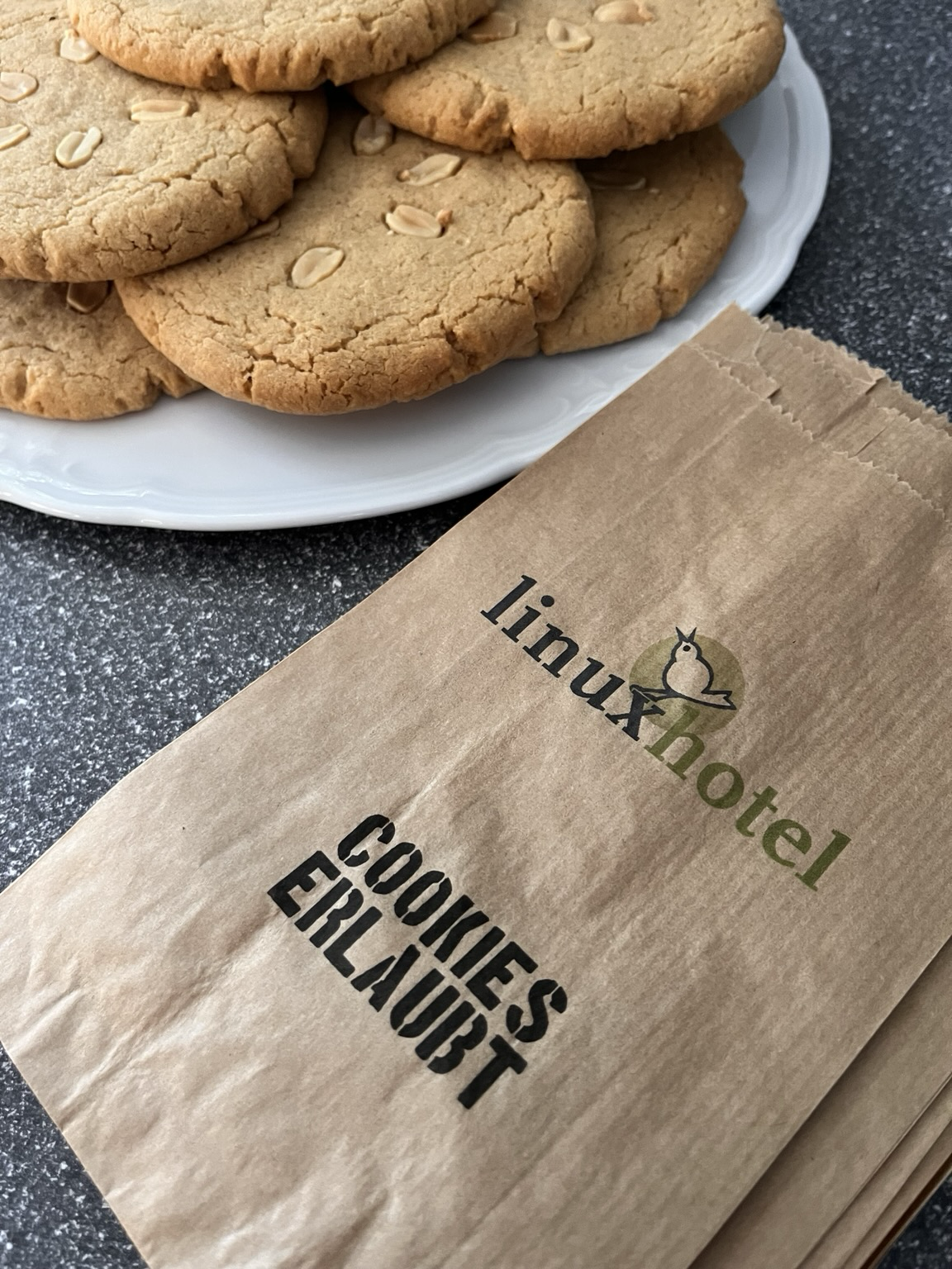Helle, große und runde Kekse auf einen Teller, daneben liegen Papiertüten bereit. Sie tragen die Aufschrift Cookies erlaubt. 